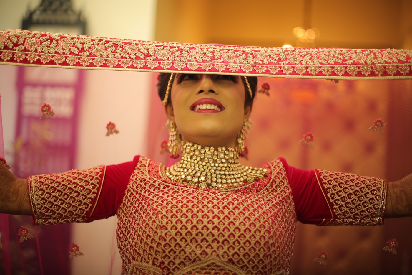 Bride beneath a red-and-gold embroidered dupatta held overhead