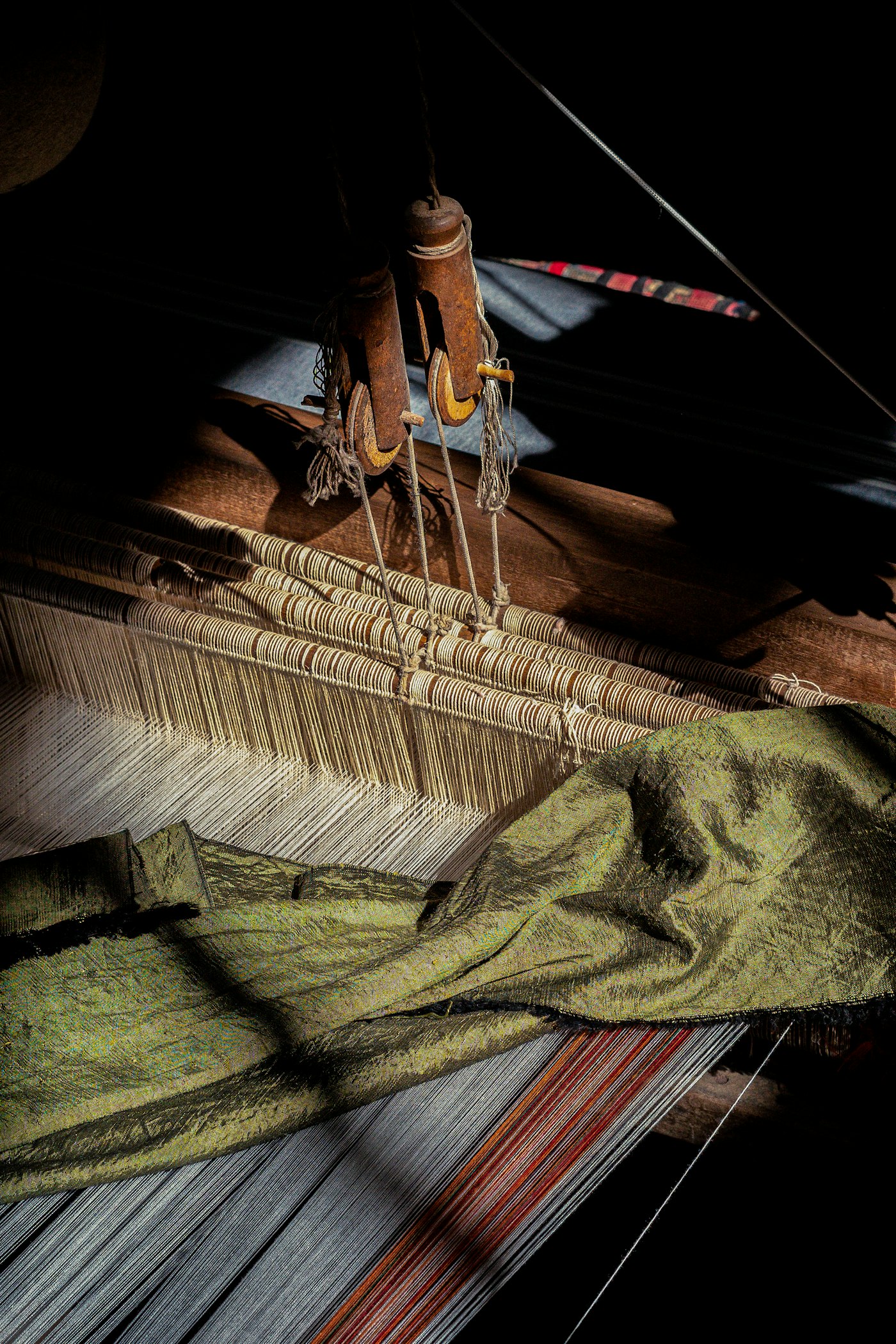 The pit loom in low light — olive silk gathered under the heddles