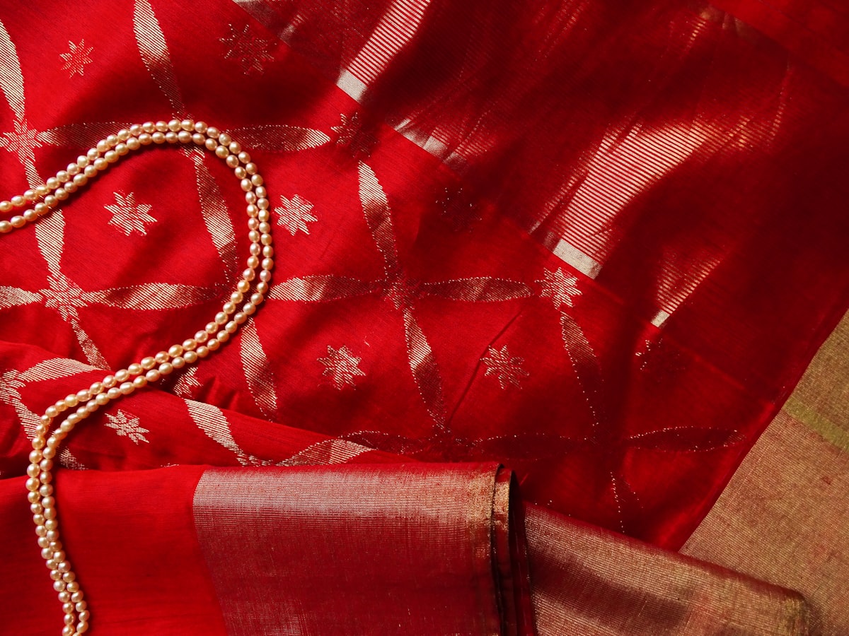 Silver zari stars woven into red silk, pearls resting on the border